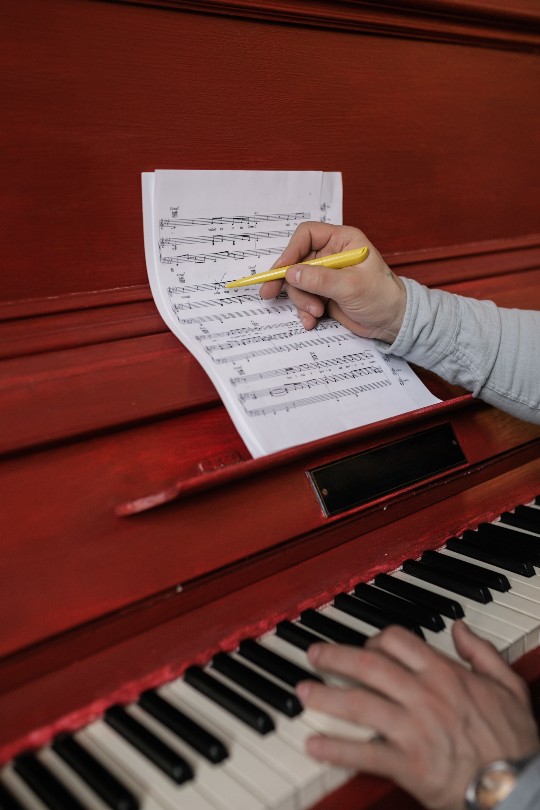 Person schreibt in Noten auf Klavier